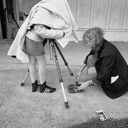 Photographer (Wendy Ewald) sits on the ground in front of Celeste, who leans against a tripod under a cover